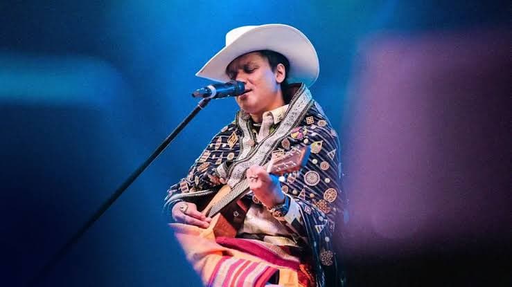 Zubeen Garg in a white hat playing guitar and singing on a blue lit stage